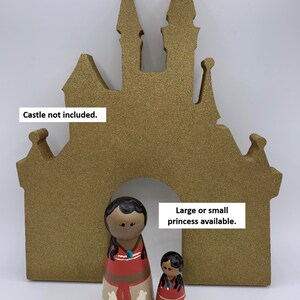 May include: Two wooden dolls dressed as a Disney princess, one large and one small, standing in front of a gold glitter castle cutout. "Large or small princess available." is written on the cutout. "Castle not included." is written at the top of the cutout.