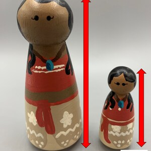 May include: Two wooden dolls, one 3.5 inches tall and the other 2 inches tall. Both dolls are painted to resemble a Polynesian woman with brown skin, black hair, and a red and white dress. The larger doll is labeled "3.5 Inches (large)" and the smaller doll is labeled "2 Inches (small)".