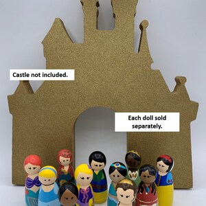 May include: A collection of 12 hand-painted wooden dolls, each depicting a different Disney princess, standing in front of a gold glitter castle cutout. Each doll sold separately. Castle not included.
