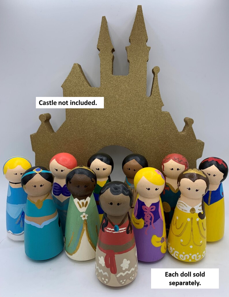 May include: A set of 11 hand-painted wooden peg dolls dressed as Disney princesses. The dolls are arranged in front of a gold castle cutout. Each doll is sold separately. "Castle not included." and "Each doll sold separately." are written in the image.