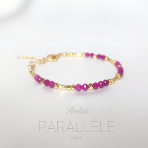 Op de afbeelding: Een delicate gouden armband met roze edelsteen kralen en gouden spacers. De armband ligt op een witte achtergrond. De tekst "Rubis PARALLÈLE PARIS" is zichtbaar onder de armband.
