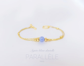 May include: A delicate gold chain bracelet with a light blue agate bead. The bracelet has a toggle clasp and is layered with two chains.