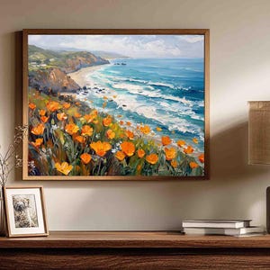 May include: A framed landscape painting shows a coastal scene with bright orange flowers. The artwork features a beach, ocean waves, and a blue sky. The painting is displayed above a wooden table.