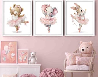 May include: Three framed watercolor prints of dancing animals: a bear, an elephant, and a bunny, all wearing pink tutus and ballet shoes. The prints are displayed above a white dresser with additional pink decor, including a teddy bear and pillows, creating a soft, whimsical nursery theme.