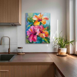 May include: A vibrant floral painting featuring two hibiscus flowers in shades of pink, orange, and yellow. The artwork showcases a close-up view of the blossoms with green leaves against a blue and green background. The painting is displayed on a white wall.