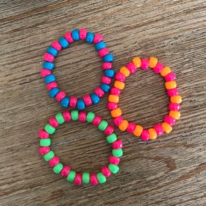Könnte beinhalten: Drei bunte Perlenarmbänder. Die Armbänder bestehen aus kleinen, runden Perlen in den Farben Blau, Orange und Grün.