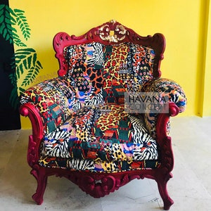Pu&ograve; includere: Una poltrona rossa ornata con un rivestimento in tessuto a motivi colorati, tra cui stampe animalier, motivi geometrici e motivi tribali. La poltrona ha uno schienale alto e dettagli intagliati. Il testo "HAVANA CONCEPT" &egrave; visibile sulla poltrona.
