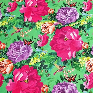 Op de afbeelding: Een groene stof met een bloemenprint met roze, paarse en oranje bloemen, kolibries en libellen.