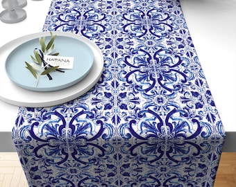 May include: Blue and white table runner with a traditional Portuguese tile pattern. The runner is made of fabric and has a smooth texture. The runner is 14 inches wide and 70 inches long.