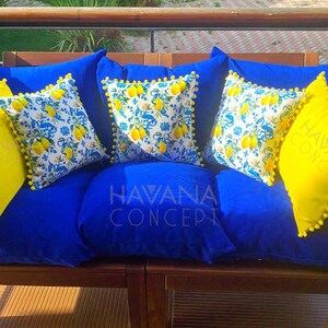 May include: A blue couch with yellow and white patterned throw pillows. The pillows have a pom-pom trim. The couch is on a wooden deck with a railing. The text "HAVANA CONCEPT" is visible on the couch.