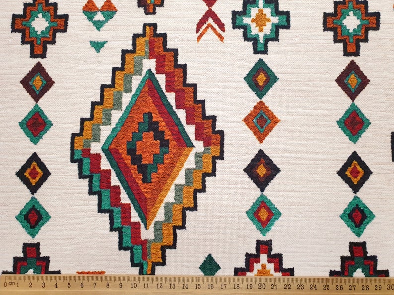 May include: White fabric with a repeating geometric pattern in shades of orange, red, green, and black. The pattern features a large diamond shape in the centre of the fabric.