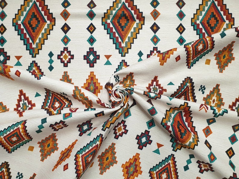 May include: White fabric with a repeating pattern of colourful geometric shapes. The pattern features a diamond shape with a smaller diamond inside, surrounded by smaller geometric shapes in shades of orange, red, teal, and brown.