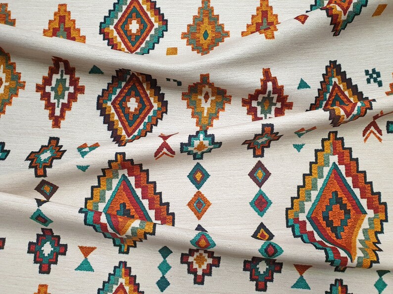 May include: White fabric with a repeating pattern of colourful geometric shapes. The shapes are in shades of orange, red, teal, and brown. The fabric has a woven texture.