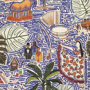 Op de afbeelding: Een kleurrijk geborduurd doek met verschillende afbeeldingen, waaronder een huis, een palmboom, een muziekinstrument en een vrouw in een blauwe jurk. Het doek bevat ook de tekst "Costurando Historias" en "Entre Nos".