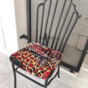 Pu&ograve; includere: Sedia in metallo nero con un cuscino di seduta a motivi colorati. Il cuscino presenta una stampa leopardata, forme geometriche e una variet&agrave; di colori, tra cui rosso, giallo e nero.