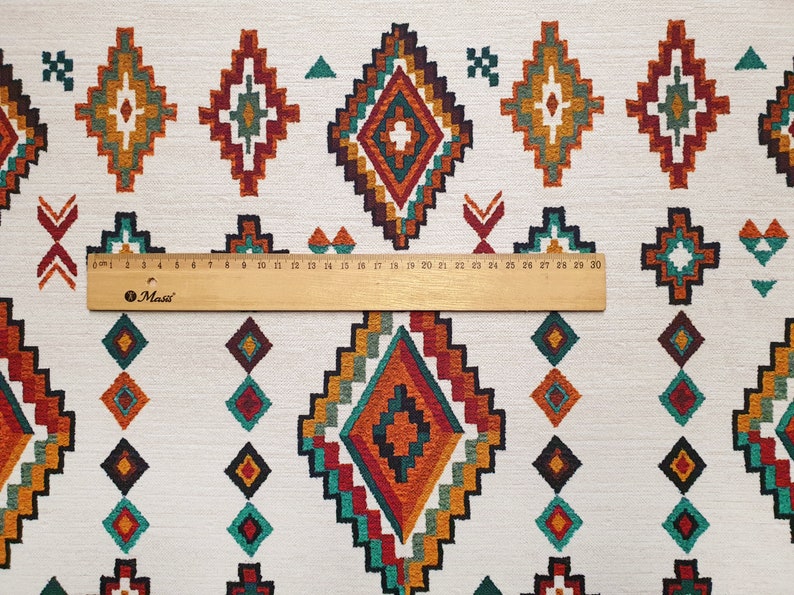 May include: White fabric with a repeating pattern of colourful diamond shapes. The diamonds are made up of a variety of colours, including red, orange, yellow, green, and blue. The fabric is measured with a ruler that shows 30 centimetres.