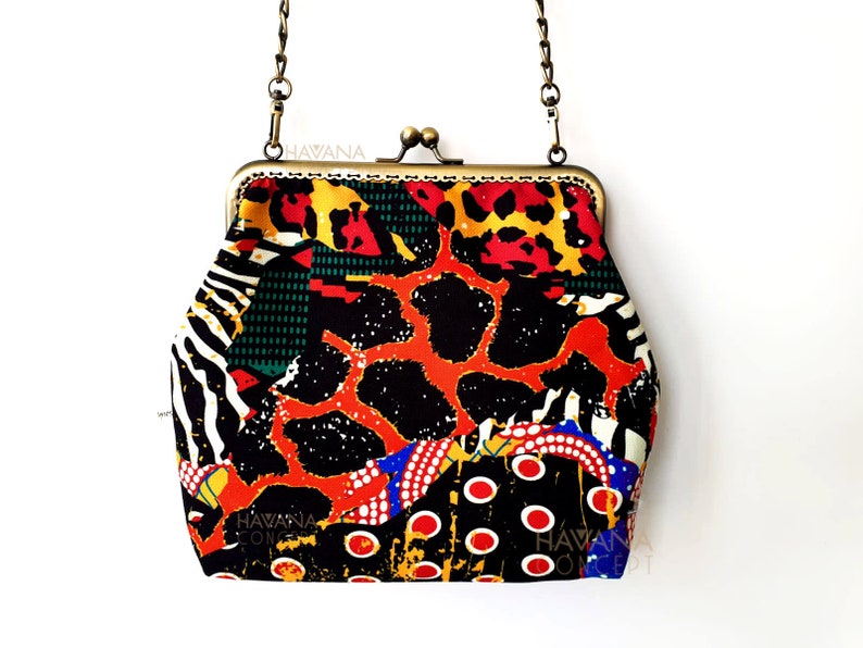 Pu&ograve; includere: Una pochette colorata con una tracolla a catena dorata. La pochette &egrave; realizzata in tessuto con sfondo nero e un motivo rosso, arancione, giallo, verde, bianco e blu. La pochette ha una chiusura a scatto e il testo "HAVANA" &egrave; stampato sul davanti.