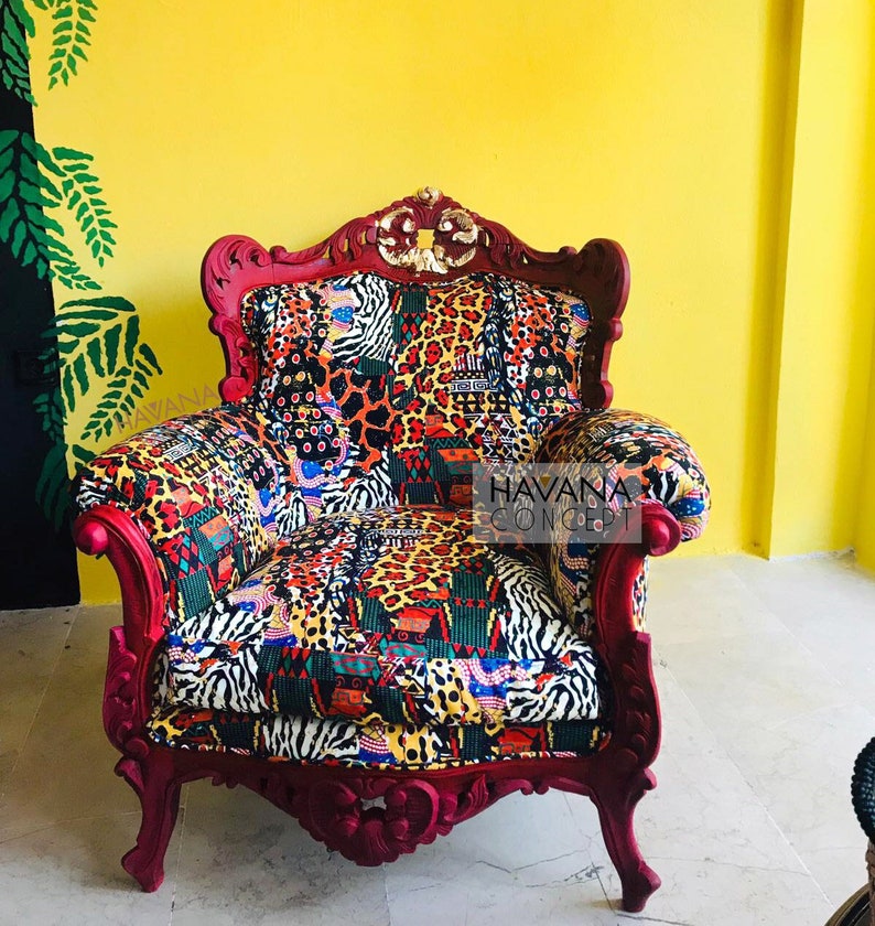 Pu&ograve; includere: Una poltrona rossa ornata con un rivestimento in tessuto a motivi colorati, tra cui stampe animalier, motivi geometrici e motivi tribali. La poltrona ha uno schienale alto e dettagli intagliati. Il testo "HAVANA CONCEPT" &egrave; visibile sulla poltrona.