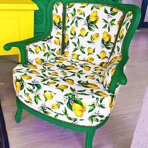 May include: A green armchair with a white and yellow lemon print upholstery. The chair has a high back and a curved seat. The chair is sitting on a wooden floor.