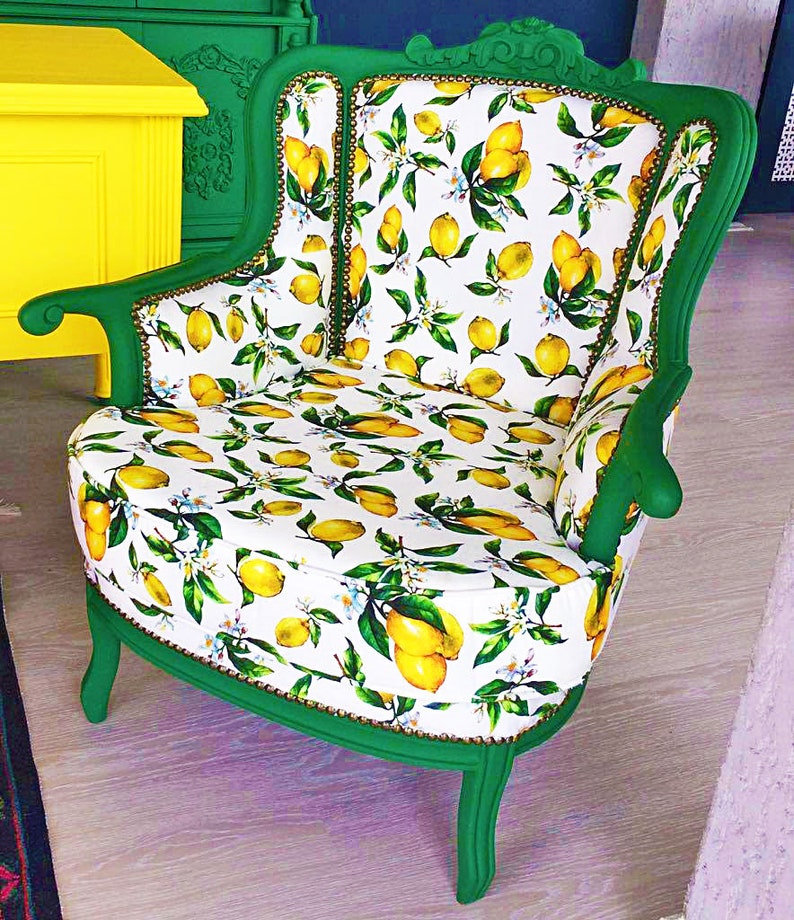 May include: A green armchair with a white and yellow lemon print upholstery. The chair has a high back and a curved seat. The chair is sitting on a wooden floor.