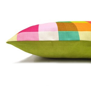 May include: A colorful pillow with a checkered pattern in shades of pink, orange, yellow, green, and brown. The pillow has a solid green back.