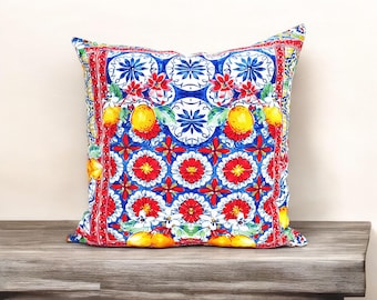 May include: A square cushion with a colourful floral and lemon pattern. The cushion has a blue background with red, yellow, and white accents. The pattern is reminiscent of Italian majolica tiles.
