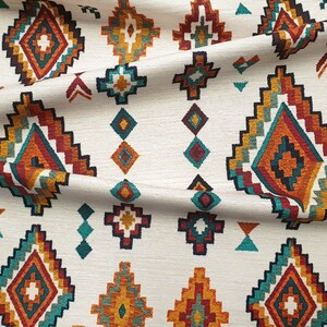 May include: White fabric with a repeating pattern of colourful geometric shapes. The pattern features a diamond shape with a smaller diamond inside, surrounded by a border of red, orange, yellow, green, and blue.