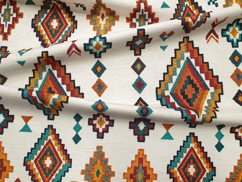 May include: White fabric with a repeating pattern of colourful geometric shapes. The pattern features a diamond shape with a smaller diamond inside, surrounded by a border of red, orange, yellow, green, and blue.