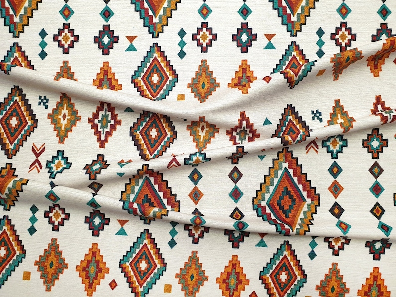 May include: White fabric with a repeating pattern of colourful geometric shapes. The pattern features a diamond shape with a smaller diamond inside, surrounded by smaller geometric shapes in shades of orange, red, teal, and black.