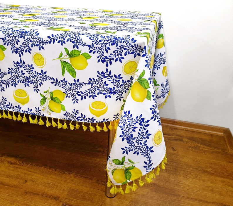 May include: White tablecloth with a lemon and blue leaf pattern. The tablecloth has yellow tassels around the edges.