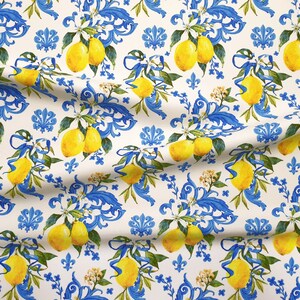 May include: A white fabric with a repeating pattern of blue and white floral designs and yellow lemons. The lemons are arranged in clusters and are surrounded by blue and white floral designs.
