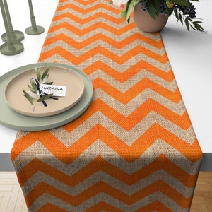 Può includere: Tovaglia da tavolo in juta con motivo a chevron arancione e beige. La tovaglia da tavolo è su un tavolo bianco con un piatto e candelieri.