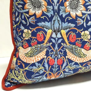 Pu&ograve; includere: Un cuscino blu con un bordo rosso presenta un motivo ripetitivo di uccelli stilizzati, fiori e foglie. Il motivo &egrave; ispirato al movimento Arts and Crafts.