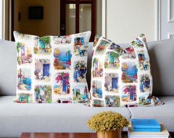 May include: Two decorative cushions on a grey sofa. Each cushion displays a collage of colourful Mediterranean scenes with doors, flowers, and sea views. The cushions add a touch of coastal charm to any living space.