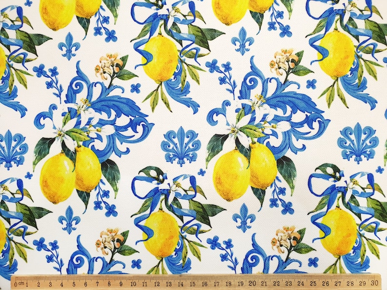 May include: White fabric with a repeating pattern of yellow lemons, blue and white floral designs, and blue and white scrollwork.