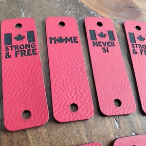 May include: Five red leather keychains with black text and a Canadian flag design. The keychains read "Strong & Free", "Home", "Never 51", "Strong & Free", and "No S".