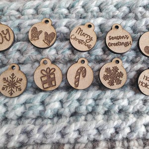 May include: Ten wooden Christmas ornaments with engraved festive designs and text. The ornaments feature a snowflake, a gift, a candy cane, and the phrases "Joy", "Merry Christmas", and "Happy Holidays".