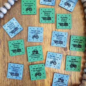May include: A selection of square patches featuring tractor designs and phrases such as "My Daddy drives a tractor" and "This boy loves his tractors." The patches are in blue and green, with black text and tractor illustrations.