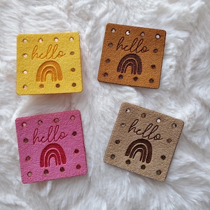 May include: Four fabric patches with a rainbow and the word "hello" in a handwritten font. The patches are in yellow, brown, pink, and beige.
