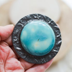 May include: A round, blue and white ceramic brooch with a textured black metal frame.