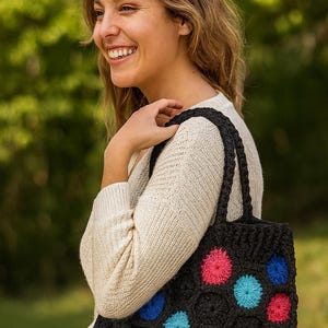 May include: Black crochet tote bag with a honeycomb pattern and colorful floral accents in pink, blue, and turquoise. The bag has two black handles and is carried over the shoulder.