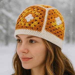 Può includere: Un cappello all'uncinetto con un motivo a granny square. Il cappello presenta una combinazione di colori giallo senape, crema e bianco. Il cappello ha un motivo floreale al centro di ogni quadrato. Il cappello è indossato da una persona.