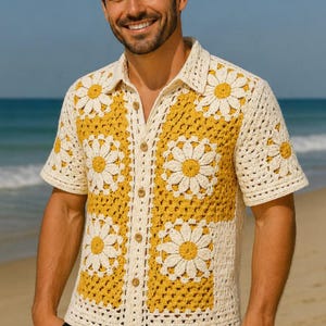 May include: Cream-colored crochet shirt with short sleeves and a daisy pattern. The shirt features a yellow background with white daisy flowers. The shirt has a button-up front and a collared neckline. The shirt is made of a soft, comfortable material.