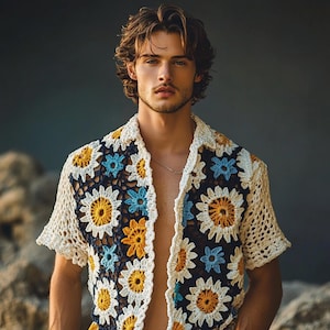 May include: A short-sleeved crochet shirt featuring a daisy pattern in yellow, blue, and white on a navy blue base. The shirt has a collar and is open at the front. The crochet work is intricate, suggesting a handmade item.
