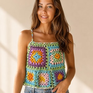 Könnte beinhalten: Ein ärmelloses Häkeloberteil aus bunten Granny-Squares in den Farben Lila, Orange, Hellblau, Rosa und Grün. Das Kleidungsstück verfügt über dünne geflochtene Träger und einen eckigen Ausschnitt, der ein lebendiges, strukturiertes Garnmuster zeigt.