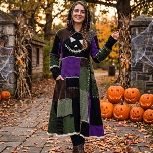 May include: A hooded, knee-length crochet dress featuring a patchwork design in black, purple, brown, and olive green. The chest displays a white stitched jack-o'-lantern face with triangular eyes and a wide, jagged, stitched mouth.