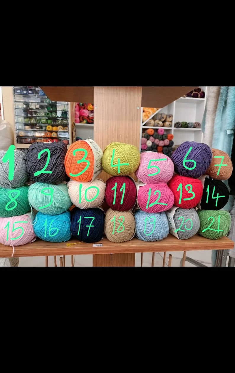 Op de afbeelding: Een display van kleurrijke bollen garen in verschillende tinten, waaronder groen, roze, blauw en oranje. Het garen is gerangschikt op houten planken, met een verscheidenheid aan kleuren en texturen, perfect voor brei- en haakprojecten.