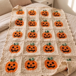 Könnte beinhalten: Eine cremefarbene Häkeldecke mit einem wiederkehrenden Gittermuster aus zwanzig einzelnen Quadraten. Jedes Quadrat enthält einen zentrierten orangefarbenen Kürbis mit schwarzem Gesicht und kleinem grünen Stiel, abgeschlossen mit einer gewellten Häkelkante.