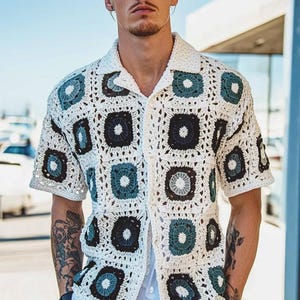 Könnte beinhalten: Ein weißes, kurzärmeliges Hemd aus Häkelarbeit mit geometrischem Muster in Blau- und Schwarztönen.