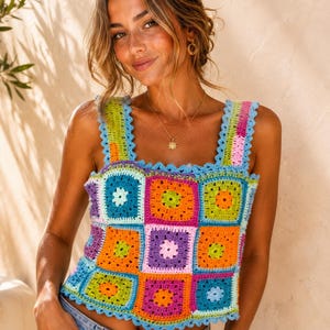 Pode incluir: Um top de crochê sem mangas com um patchwork vibrante de quadrados de crochê multicoloridos em tons de verde-limão, laranja brilhante, magenta, roxo e azul-claro. A peça possui alças largas e uma borda festonada no decote e na bainha.